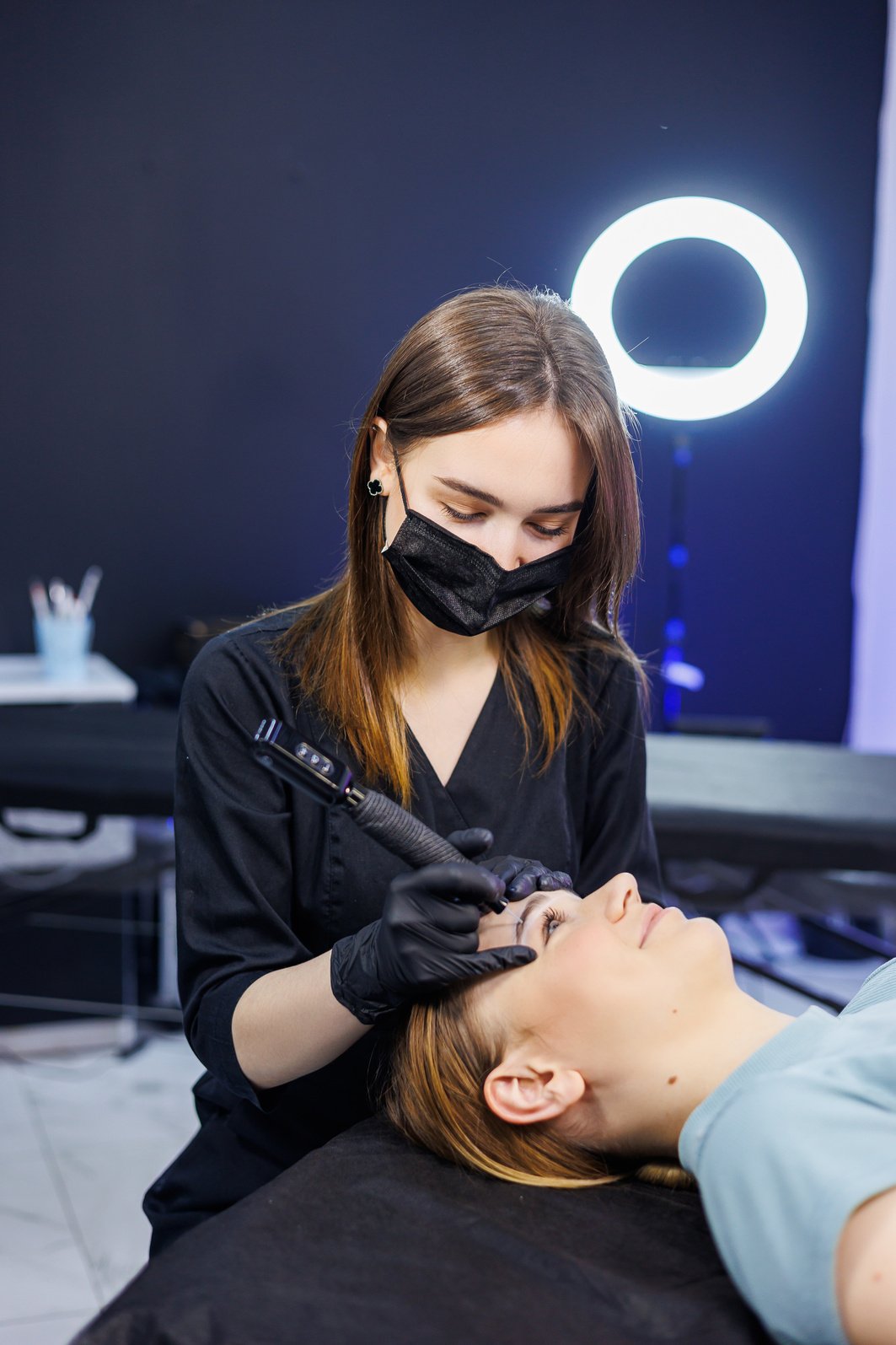 Woman professional permanent make-up artist with a permanent make-up tool. A young permanent makeup artist makes permanent eyebrow makeup